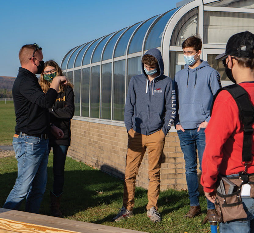 SUNY Morrisville faculty member Adam Olinski teaches Morrisville-Eaton Middle-High School students how to build raised garden beds at 18 their school.