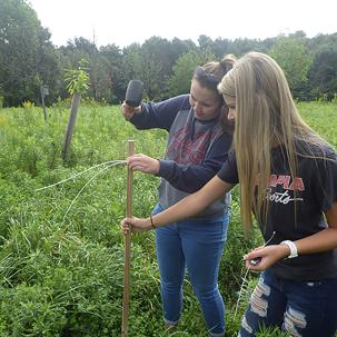 Norwich students Alexis Jaycox (center), a liberal arts major from Sherburne, and Samantha Johnson (right), an individual studies major from Norwich, set up a data logger to record temperature and humidity data as part of a climate lab for their Introduction to Biology course.